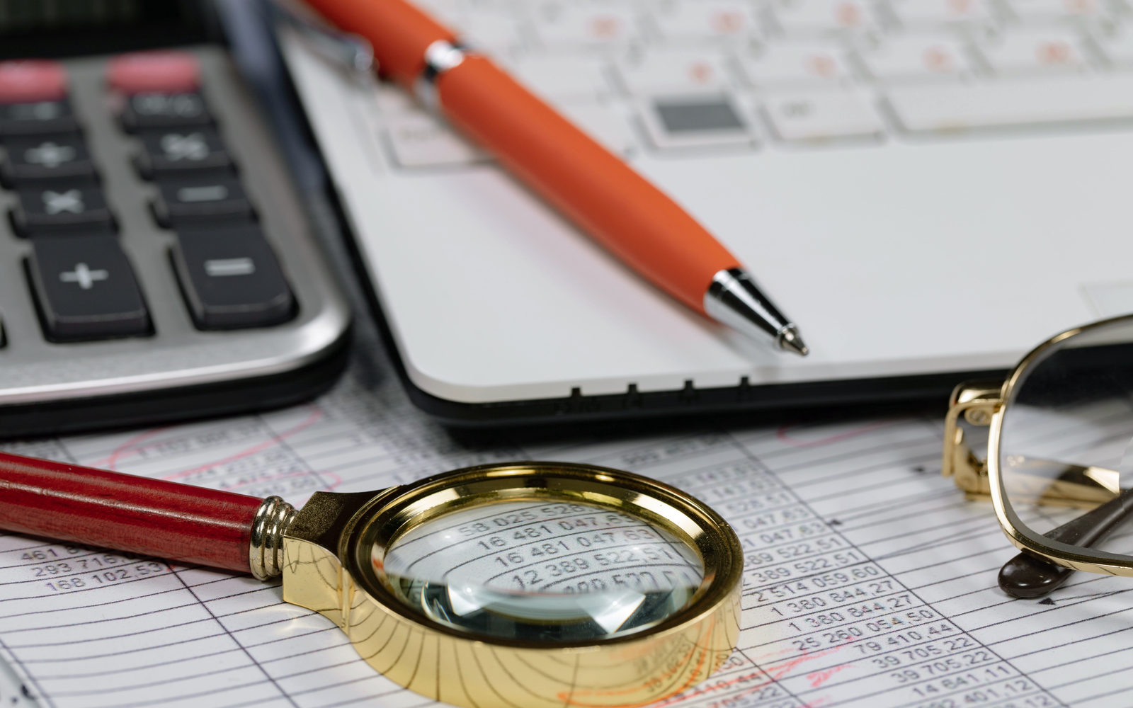 A gold magnifying glass over a financial document beside a calculator and pen