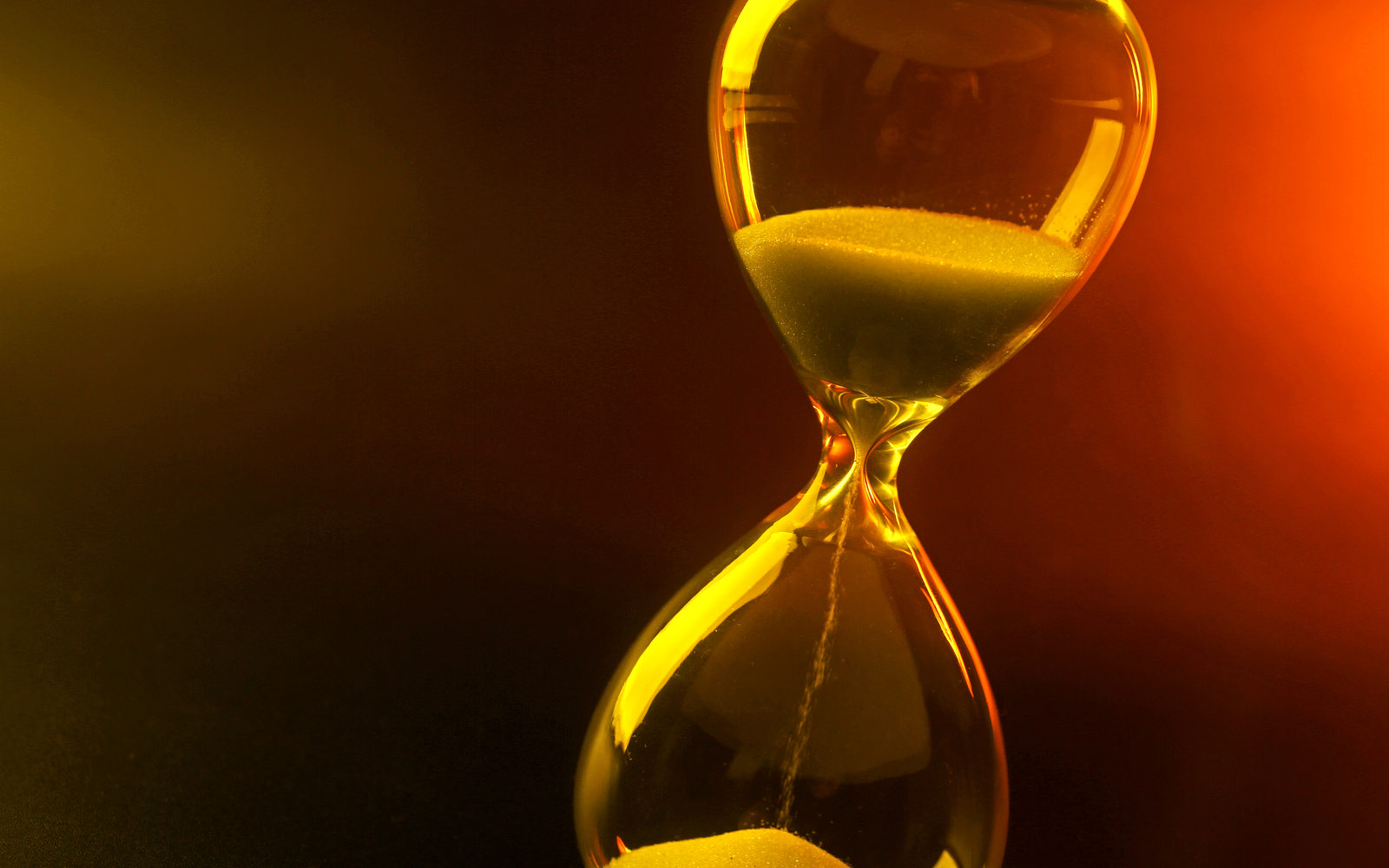 Glass hourglass with sand running through, lit in warm amber and red