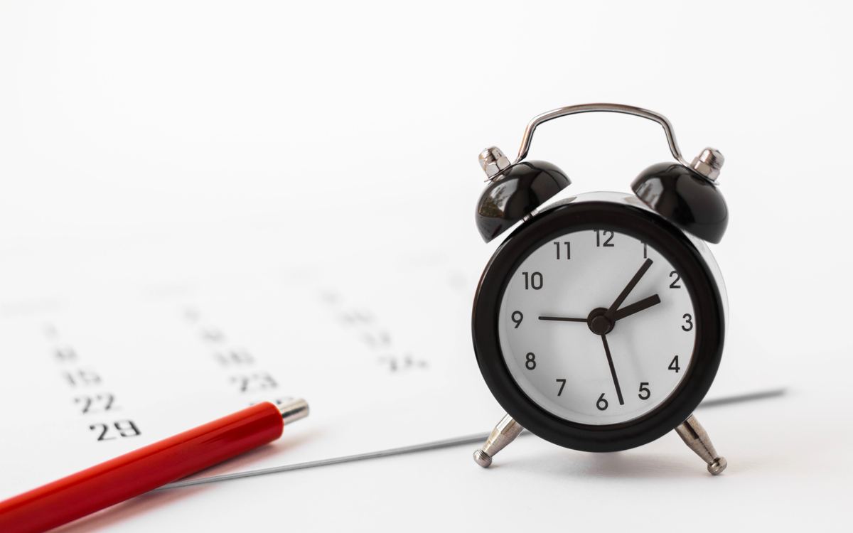 Black alarm clock standing on a printed monthly calendar beside a red pen
