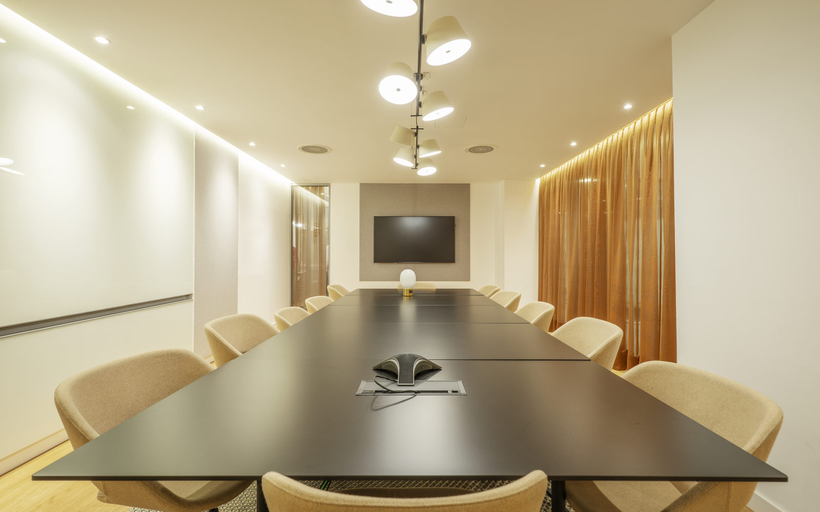 Empty modern boardroom with a long dark table, warm lighting and bronze curtains
