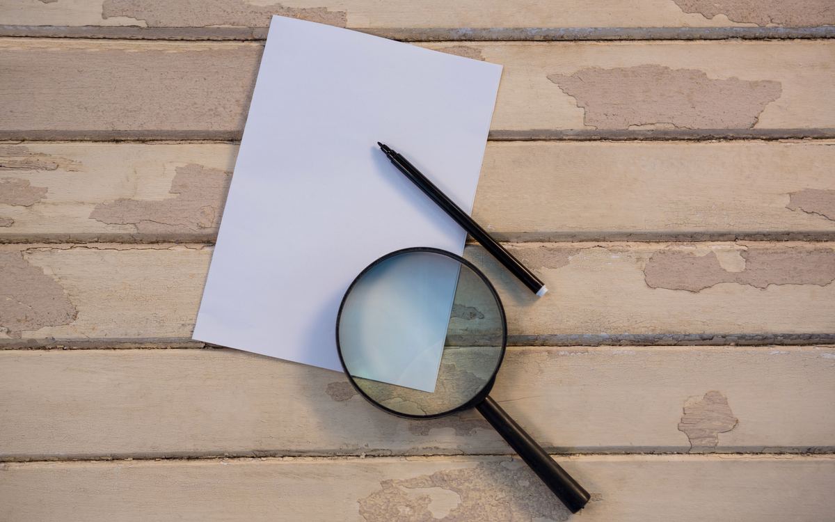 Magnifying glass and black pen on a blank sheet over weathered wooden planks