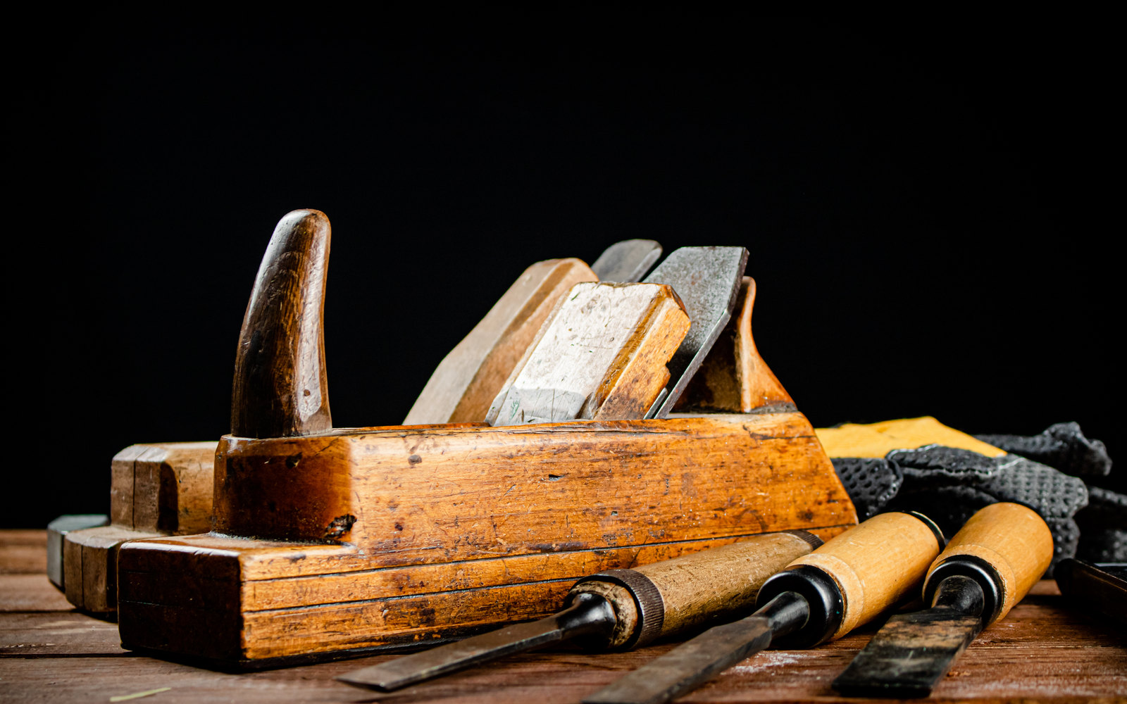 Well-worn hand plane and chisels on a workbench against a dark background