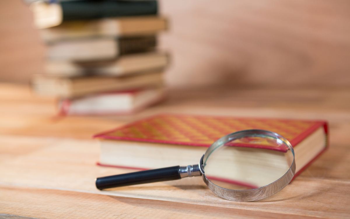 Magnifying glass resting on a red book with a stack of books behind