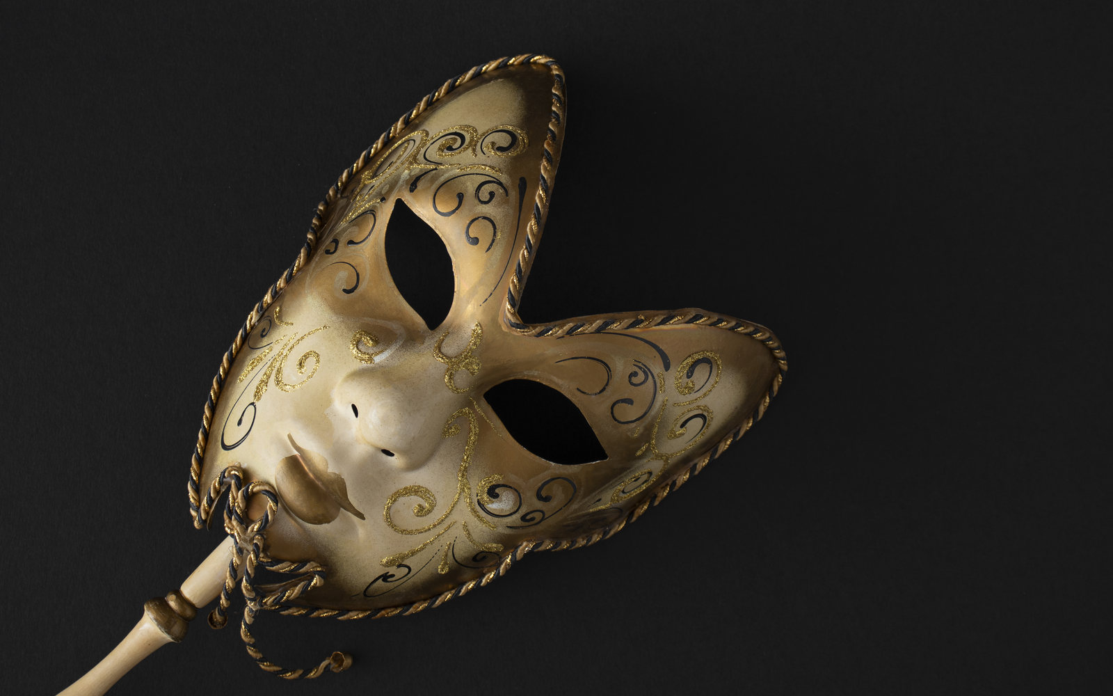 Ornate gold Venetian mask on a stick against a black background