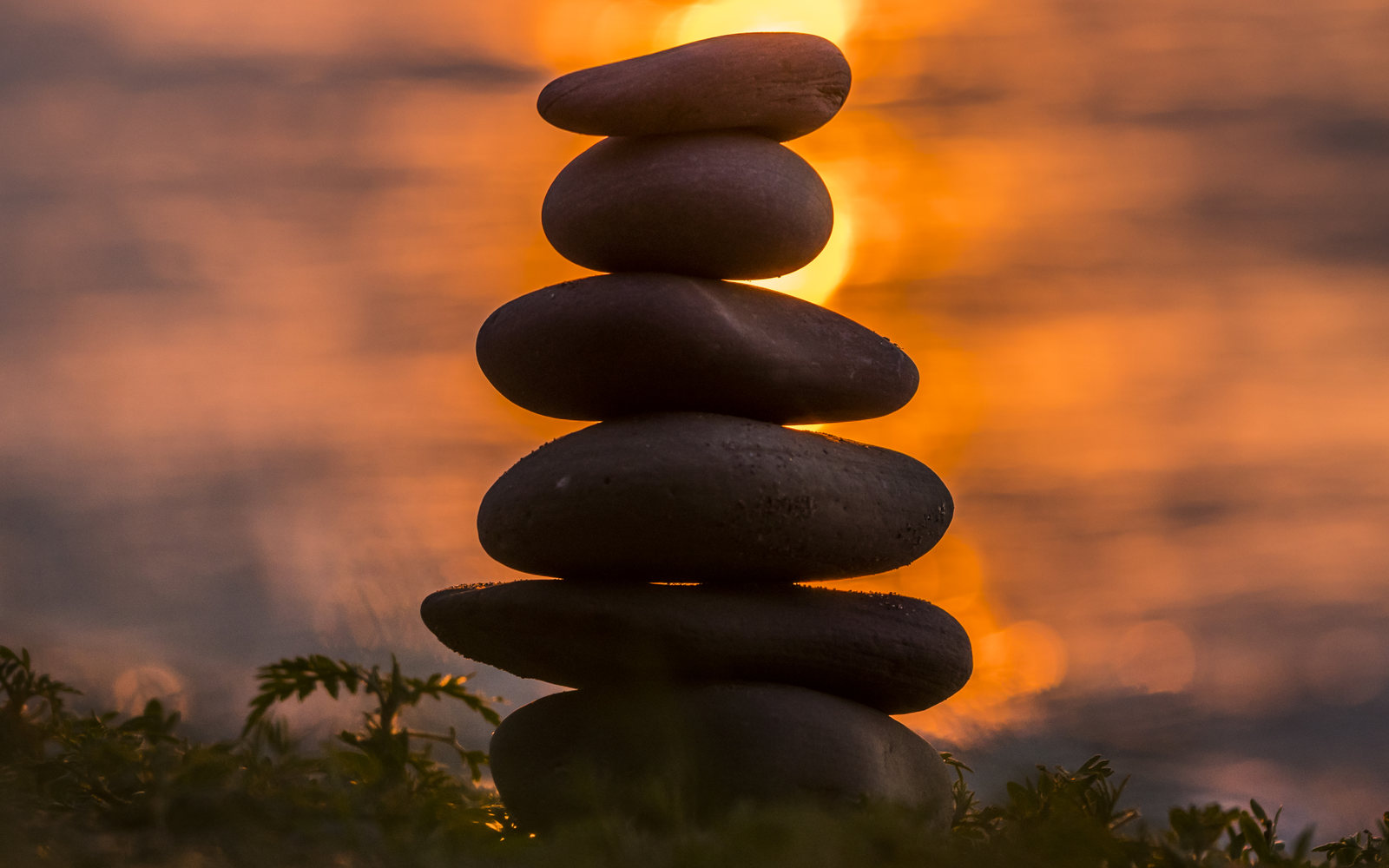 A carefully balanced stack of stones against warm orange sunset water