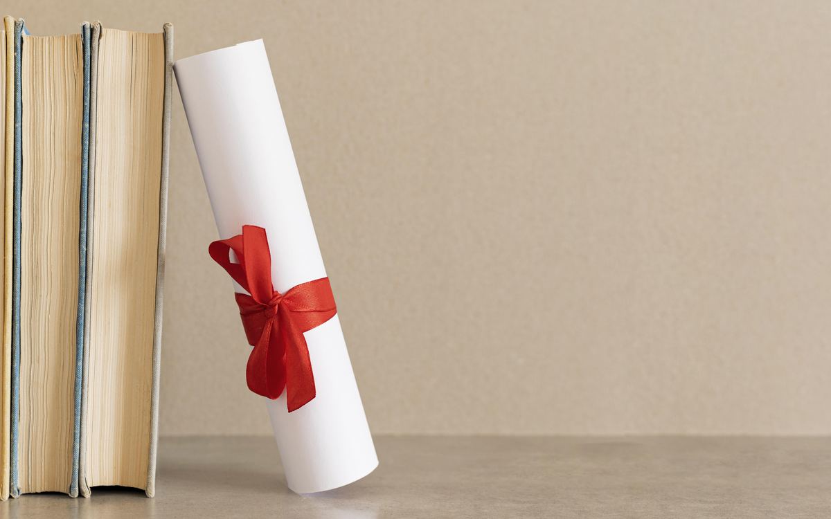 Rolled diploma tied with a red ribbon leaning against old books