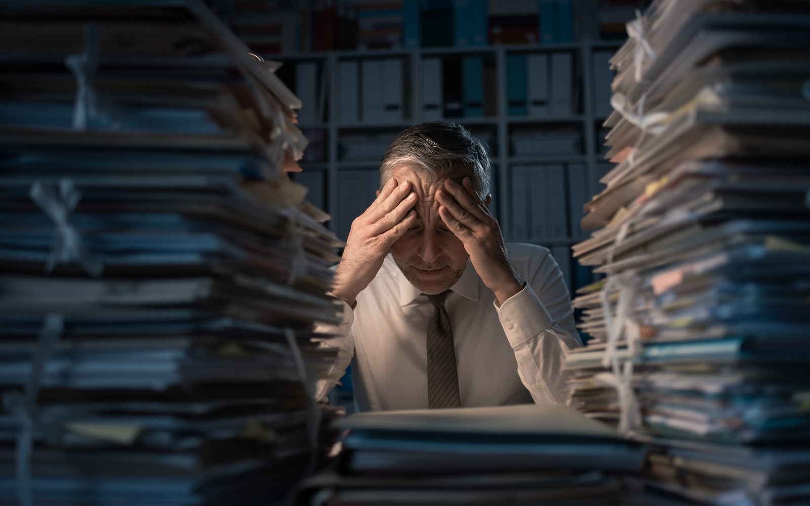 A stressed executive holding his head between towering stacks of paperwork
