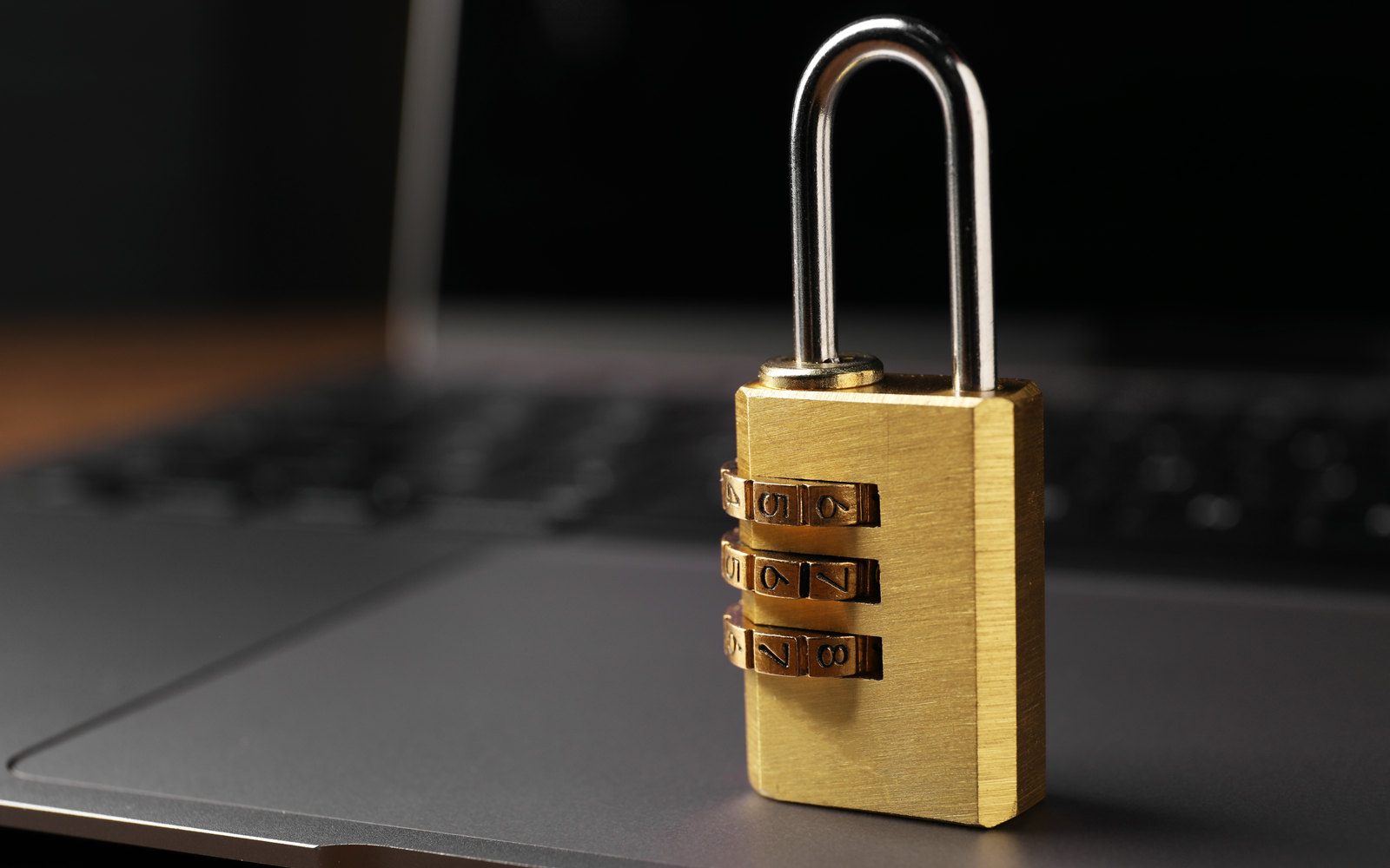 Brass combination padlock resting on a laptop in low light