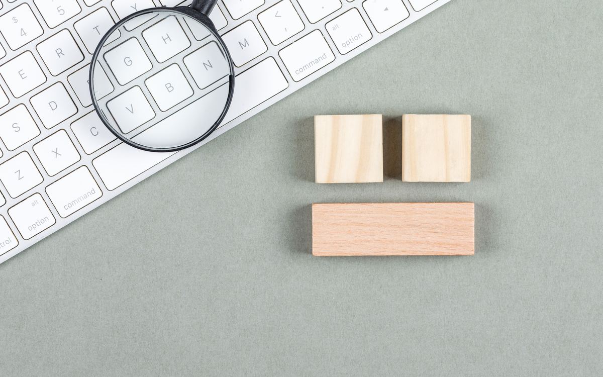 Magnifying glass on a white keyboard next to plain wooden blocks