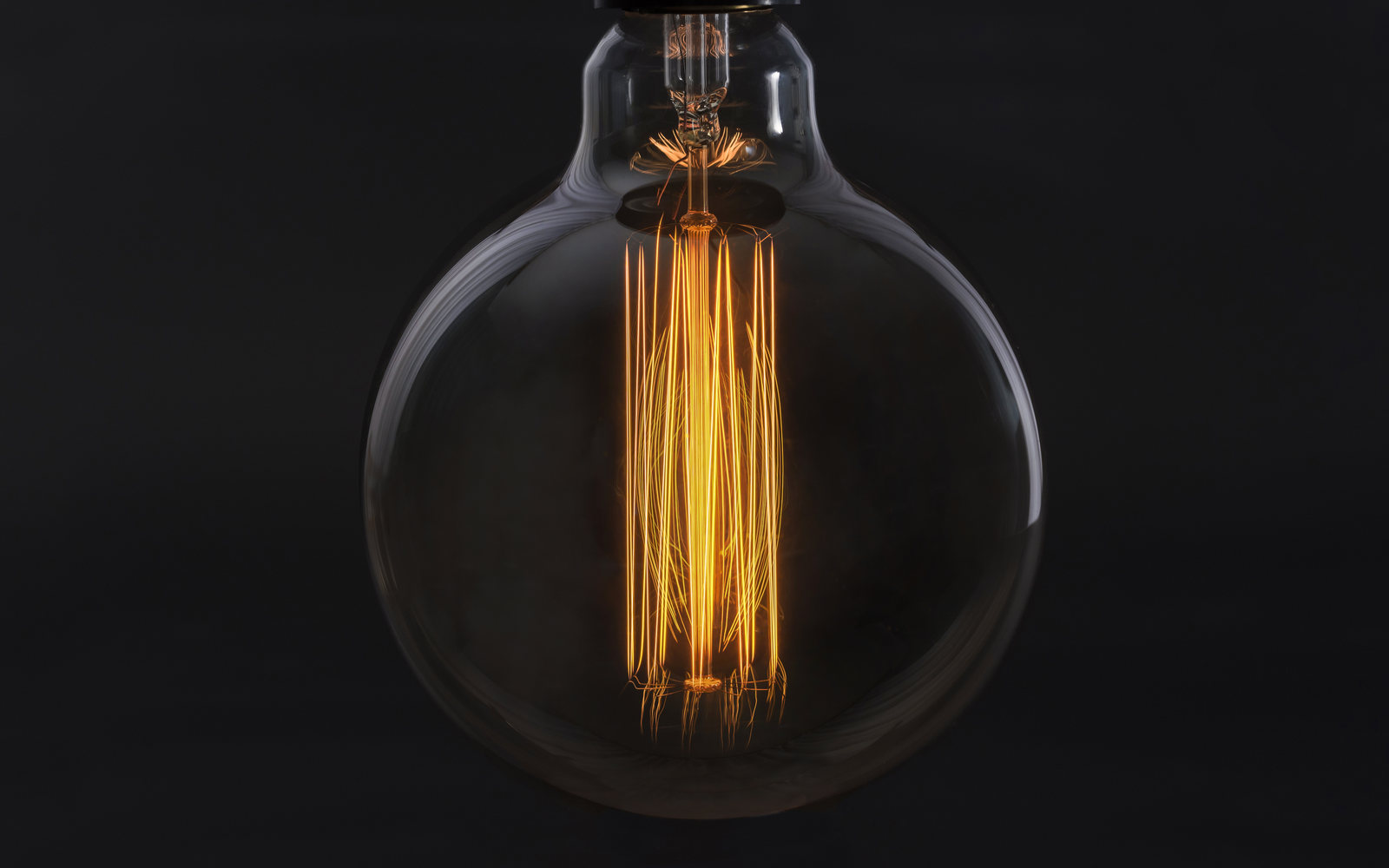 A large globe filament bulb glowing amber against a black background