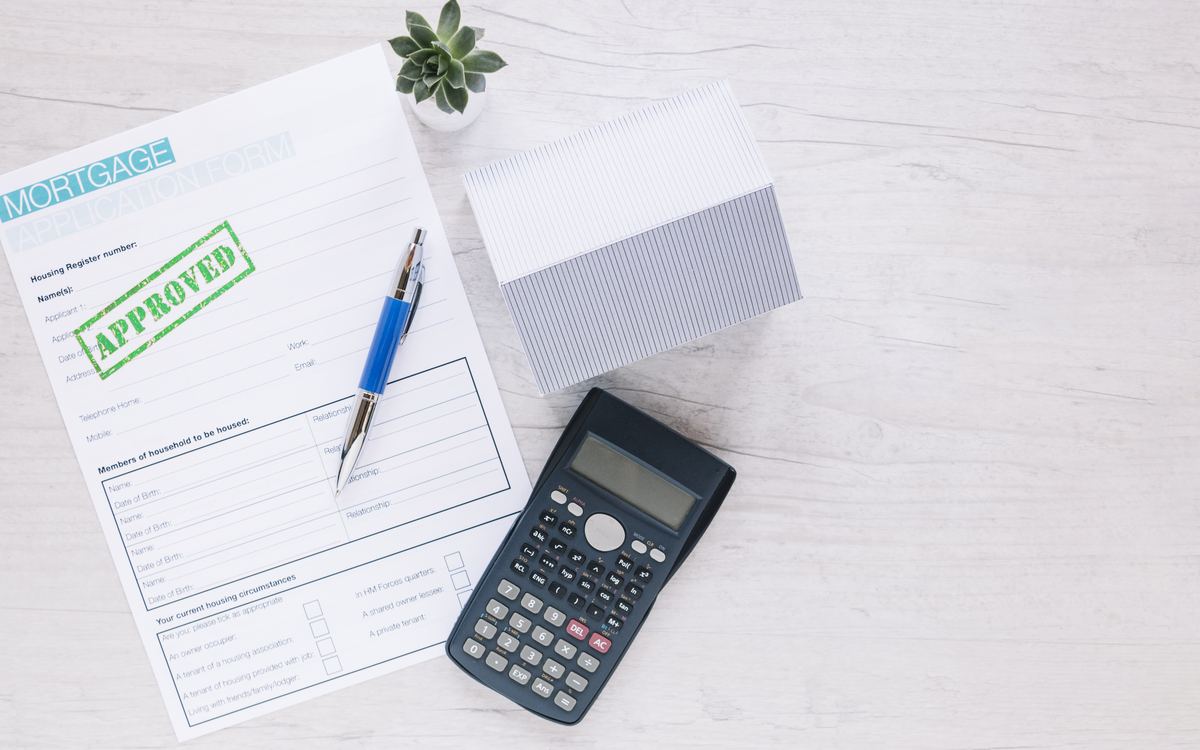 Approved mortgage application form with pen, calculator and model house on white desk