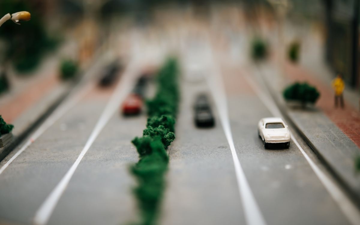 Miniature model cars driving along a tree-lined model road