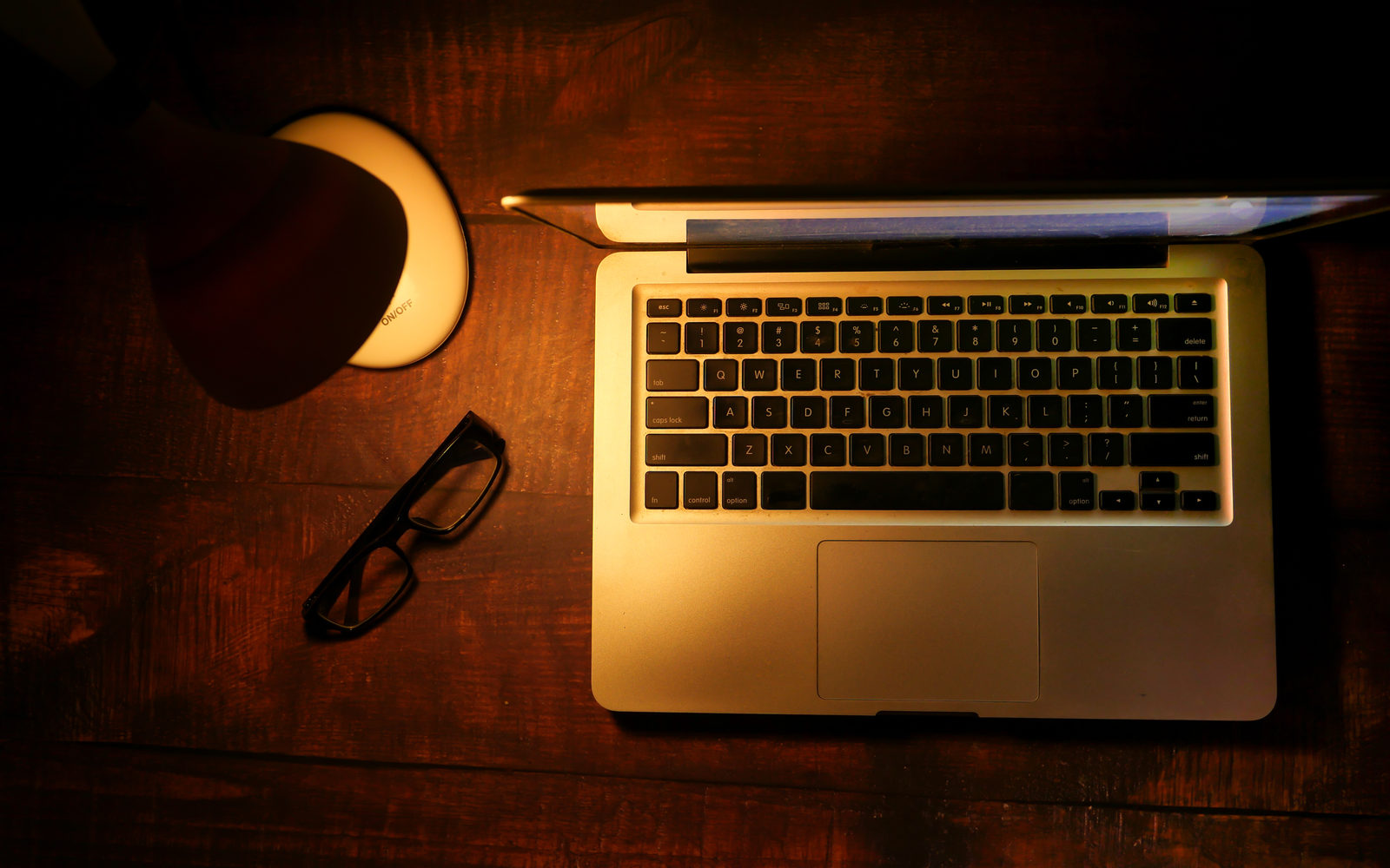 A laptop glowing on a dark desk under a warm lamp, working after hours