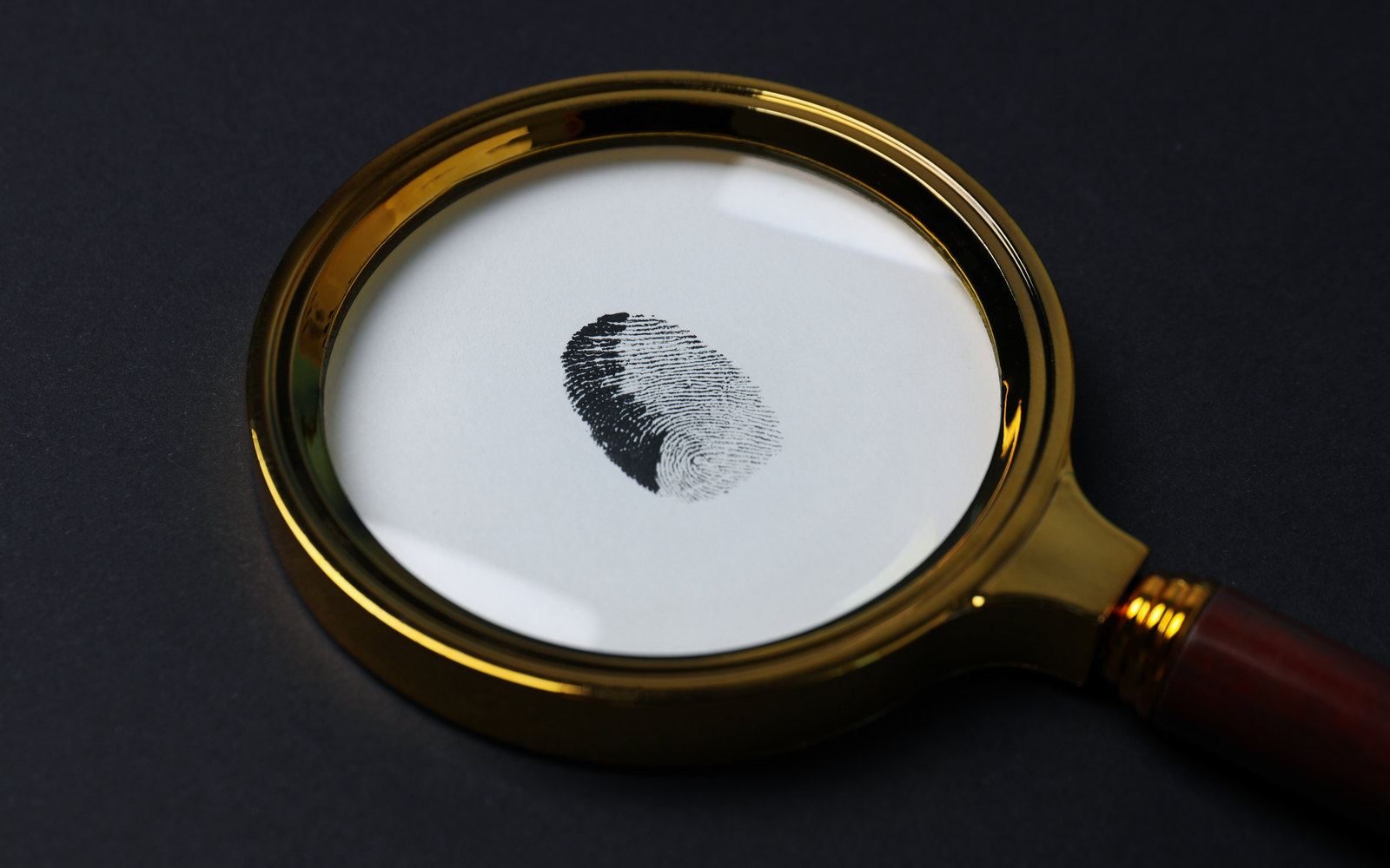 A brass magnifying glass revealing a fingerprint on paper against a dark background